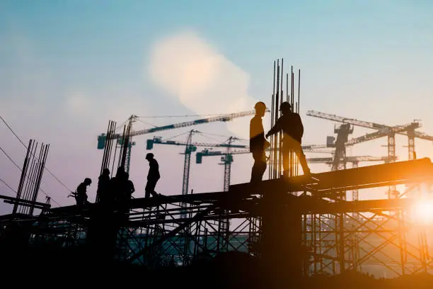 Photo of Silhouette of engineer and construction team working at site over blurred background sunset pastel for industry background with Light fair.Create from multiple reference images together.