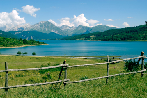 Landscape of the Lake of Campotosto (L'Aquila, Abruzzi, Italy) with wooden fence in foreground and the mountains in background under a blue clear sky in a bright summer day.