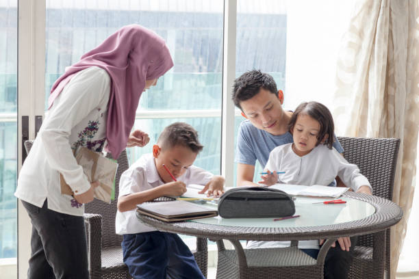 Malay parents with young boy and girl doing homework A Malay mother and father with his son and daughter in school uniforms at the dining table doing homework malay stock pictures, royalty-free photos & images