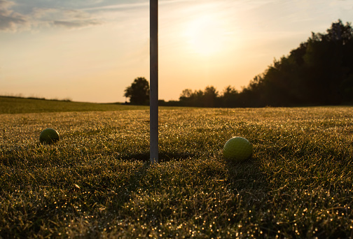 Deatil of golf course with two balls near flag in sunrise
