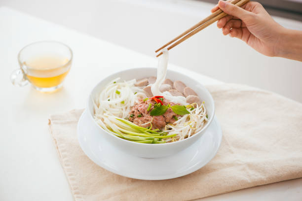 Woman eating traditional Vietnamese Pho noodle using chopsticks.