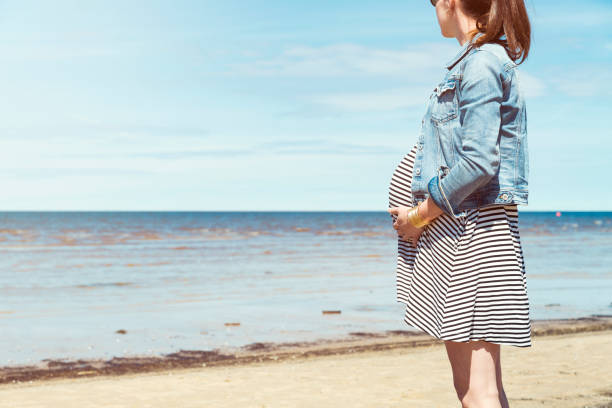 Beautiful pregnant woman standing on the beach. Pregnant woman taking a walk by the beach stock photo