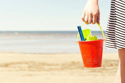 Woman holding bucket with children's beach toys - spade and shovel on a sunny day