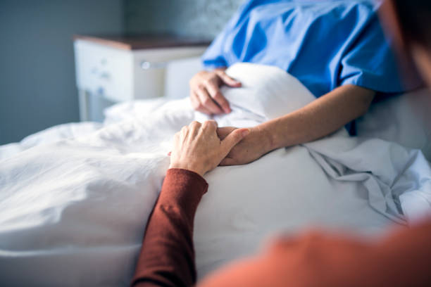 Woman holding hand of sister in hospital bed Cropped image of mature woman holding hand of sick sister in hospital bed. Female is consoling patient in ward. They are in hospital. sad gay stock pictures, royalty-free photos & images