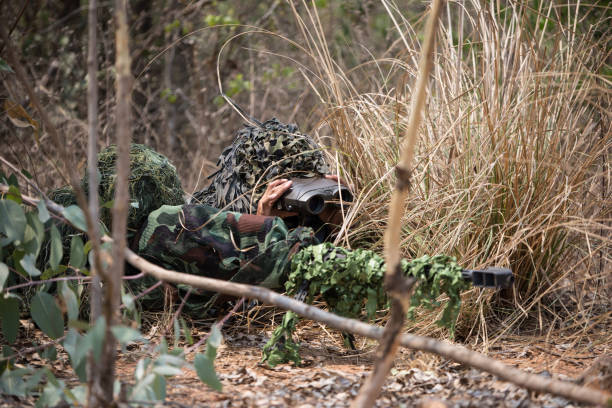 Sniper aiming G-3 rifle under camuflage tent