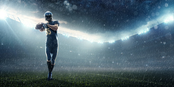 American football player catches the ball in professional sport stadium with smoke, rain and fog. Sportsman dressed in blue sport uniform