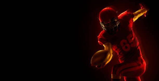 jogador de futebol americano com bola sobre um fundo vermelho escuro - football player american football sport professional sport - fotografias e filmes do acervo