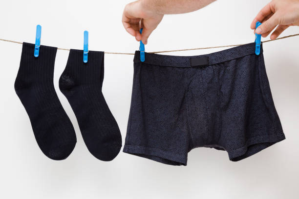 mani dell'uomo appese calzini neri puliti e pantaloncini boxer. biancheria intima asciugatura su corda da bucato a parete bianca. lavaggio a secco. lavaggio regolare. routine quotidiana. cura dei vestiti. - hanging clothesline businessman people foto e immagini stock