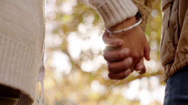 4k video footage of an unrecognizable couple holding hands and walking outdoors in a public park