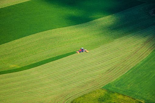 Red tractor working on beautiful green field in summer - bird eye perspective