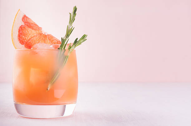 istock Summer cold cocktail with ice cubes, juice and slices grapefruit on pastel pink background. 981526644