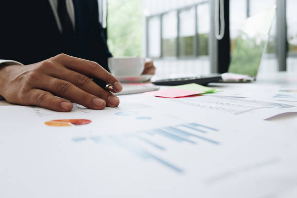 istock Data analyzing. Close up of business man adviser using pen pointing document report and discussing while hand holding a cup of coffee in his office 981533230