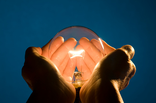Holding Energy in the Palms of my Hands, displays a clear incandescent light bulb position in the open hands of a woman  