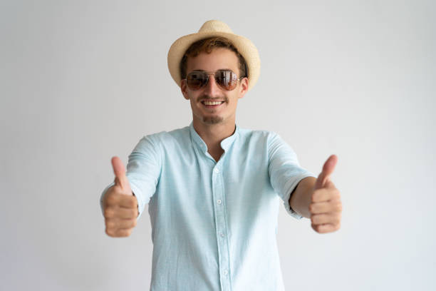 Happy enjoyable handsome guy showing thumbs-up and having fun on vacation. Cheerful young man in sunglasses smiling at camera. Summer holidays concept