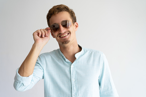 Portrait of happy blonde guy wearing sunglasses. Young Caucasian stylish man adjusting glasses and smiling at camera. Summer outfit concept