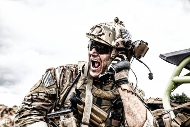 Soldier communicating with command during battle Special forces soldier, military communications operator or maintainer in helmet and glasses, screaming in radio during battle in desert. Calling up reinforcements, reporting situation on battlefield militant groups photos stock pictures, royalty-free photos & images
