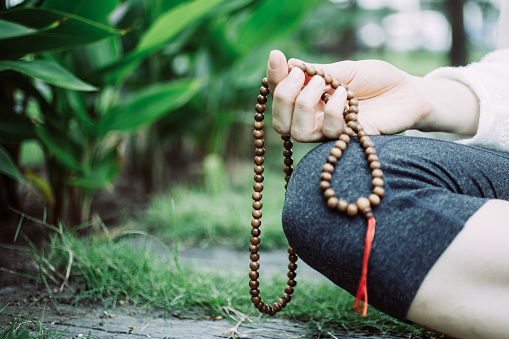 Close-up of female hand sitting, holding rosary beads and meditating outdoors