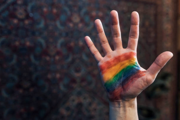 Top view of Person having  rainbow on hand palm for St Valentine's Day. Closeup of a young Caucasian man with rainbow flag painted in his palm, emerging from darkness.