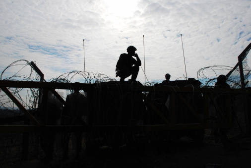 Israeli soldiers guarding a barrier, silhouetted against afternoon sun