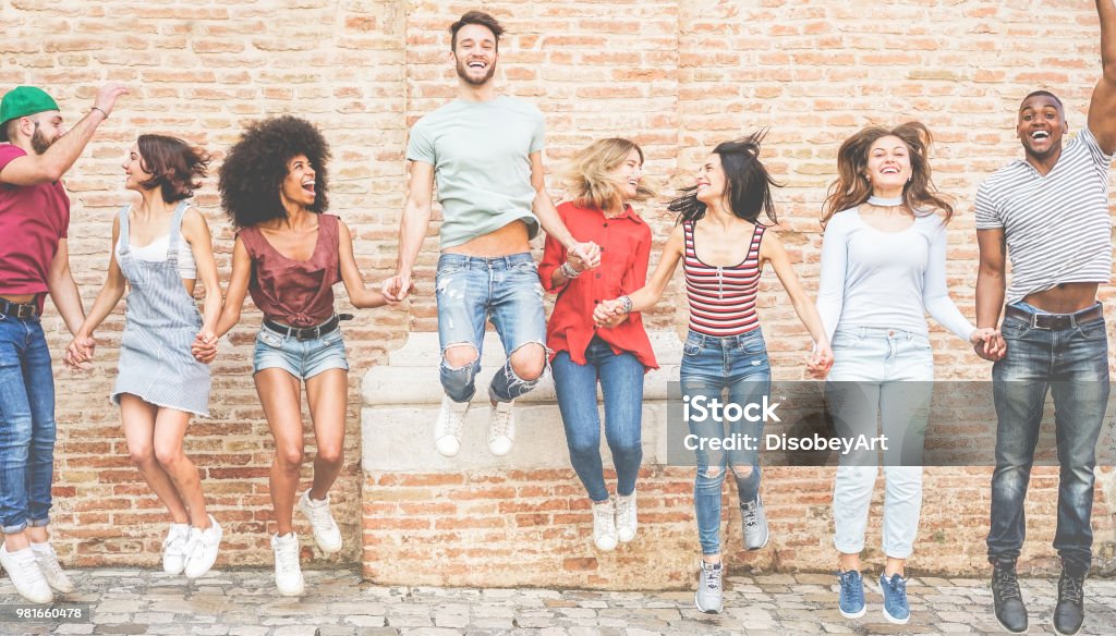 Happy millennials friends jumping outdoor - Young people having fun together - Youth lifestyle, team, multiracial, friendship concept - Main focus on center guys Multiracial Group Stock Photo