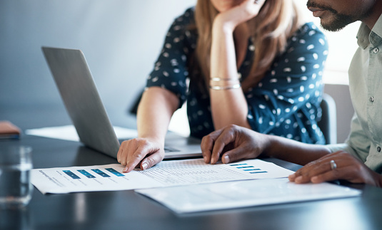 Cropped shot of a businessman and businesswoman using a laptop while going through paperwork together in a modern office