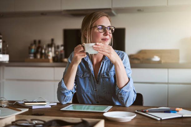 uśmiejąca kobietę pijącą kawę podczas pracy online z domu - biała kobieta czyta w okularach zdjęcia i obrazy z banku zdjęć