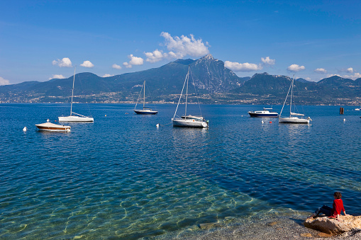Clear water, boats rocking gently on rippling water, a woman looking towards the profile of the mountains across the lake: this is a beautiful spring day! Torri del Benaco, Lake Garda, Italy. Canon EOS 5D Mark II