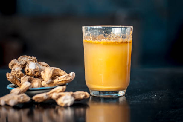 Dried ginger or Zingiber officinale or Soth,Sonth with ayurvedic medicinal extracted juice in a transparent glass on wooden surface improves the digestion and decreases the chances of cancer,diabetes.