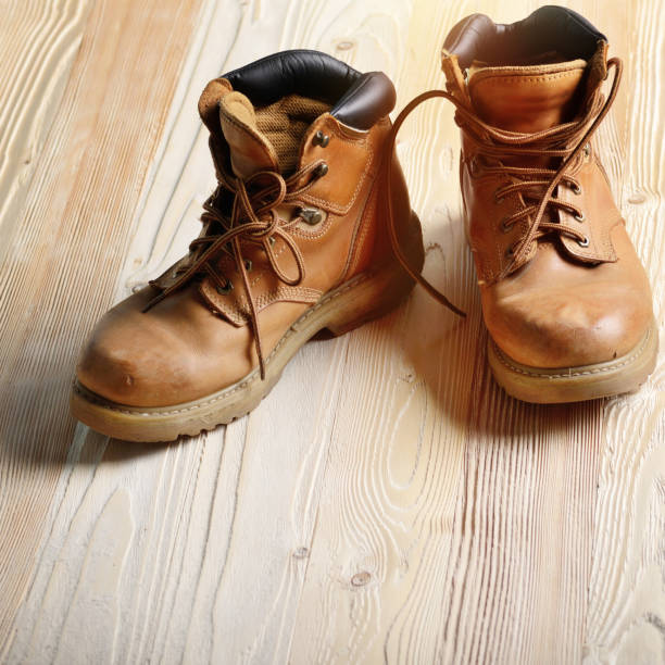 istock Yellow leather used work boots on wooden background closeup. Place for text 981766166