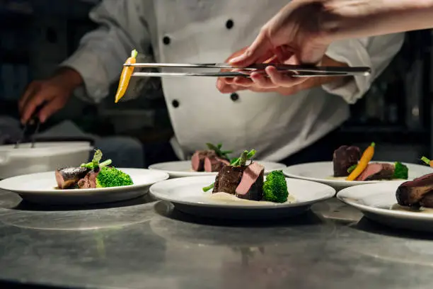 Chef’s working together to prepare multiple dishes ready for service. Colour, horizontal with some copy space. Photographed in a restaurant on the island of Møn in Denmark.