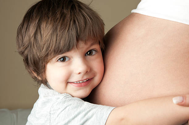 Two years old boy embracing the baby belly of his unrecognizable pregnant mother.