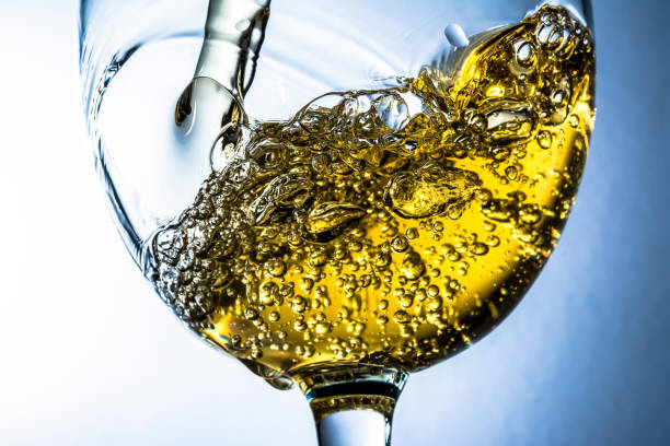 istock Stream of white wine pouring into a glass, white wine splash on grey background 981789508