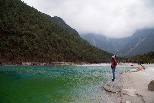 Tourist woman standing on the rock and enjoy with beautiful view of Blue Moon valley land mark in Yulong snow mountaind natural park in Lijiang city, China