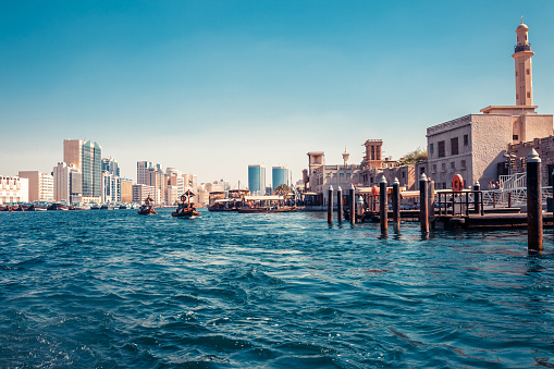 Skyline view of Dubai Creek with traditional boats and piers. Sunny summer day. Famous tourist destination in UAE.