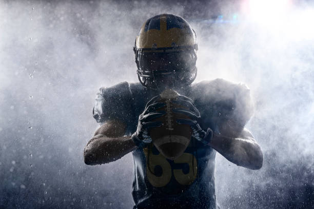 American football player in a haze and rain on black background. Portrait American football player in a haze and rain on black background. Portrait. Athlete dissecting white smoke and water drops. Sportsman shines in the rays of light aggression photos stock pictures, royalty-free photos & images