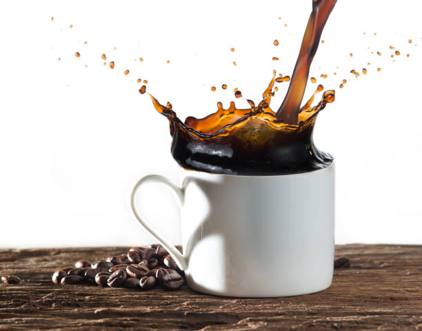 istock Coffee splash with heart shaped handle shadow and coffee beans on wood 981855268