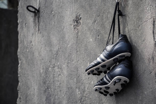 scarpe da calcio appese a un muro di cemento grezzo. - stud foto e immagini stock