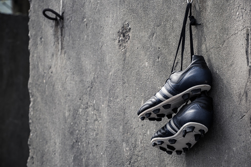Soccer shoes hanging on a rough concrete wall.