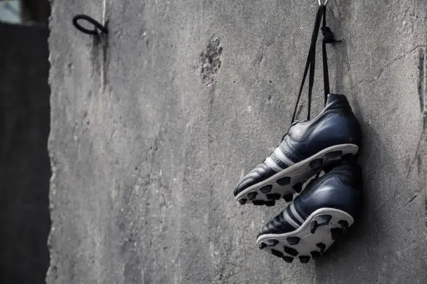 Photo of Soccer shoes hanging on a rough concrete wall.