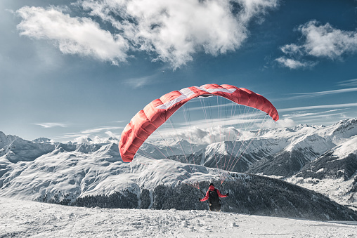 A grayscale of a man paragliding, his parachute billowing in the wind