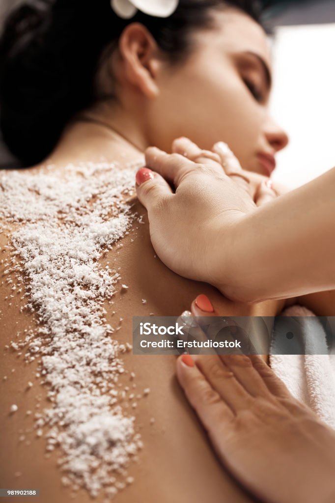woman receiving massage with salt peeling Relaxed beautiful young woman receiving massage with salt peeling in spa salon. Beauty treatment Exfoliation Stock Photo