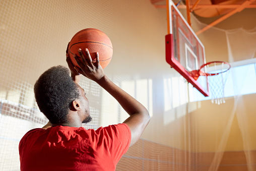 Anonymous African-American sportsman preparing to shoot goal while playing basketball in gym.