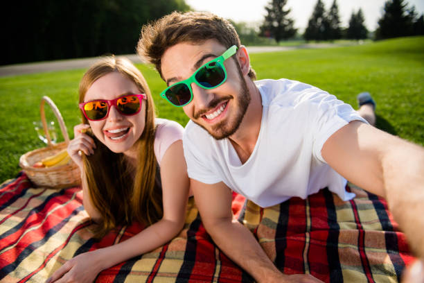 autoportrait de funky frère fou gai et sœur se trouvant sur le vert gazon outdoor selfie tir sur caméra frontale ayant appel vidéo bénéficiant soleil ayant l’atmosphère de bonne humeur - glasses grass women lying on front photos et images de collection