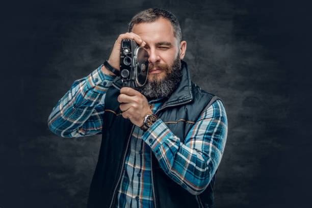 istock Bearded middle age male holds vintage 8 mm video camera. 982003232