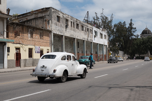 Havana, Cuba - 28 April 2018: Cuban man jaywalking across the street in Havana as a several classic 1950s American cars drive by on the road in Havana.