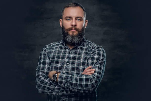 Middle age male in plaid shirt. Portrait of serious middle age bearded male dressed in plaid flannel shirt over grey background. man beard plaid shirt stock pictures, royalty-free photos & images