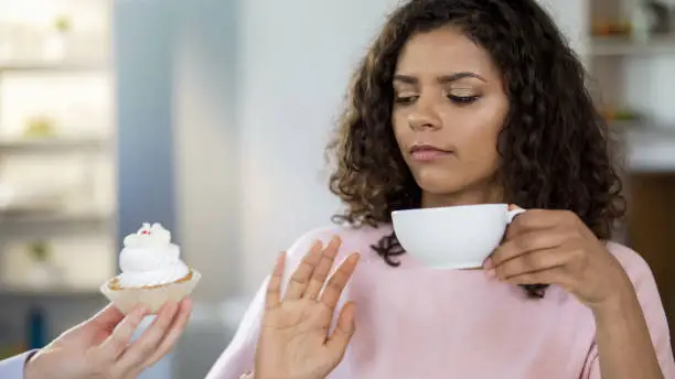 Attractive young woman drinking tea, saying no to cream-cake, healthy dieting
