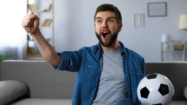 Cheerful guy loudly screaming watching football match, successful game result