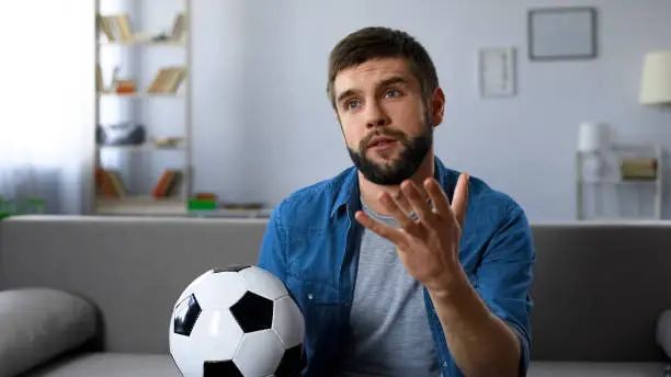 Photo of Young man nervously watching football match on tv home, frustrated at team loss