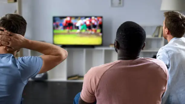 Friends nervously watching american football competition on screen, sofa experts